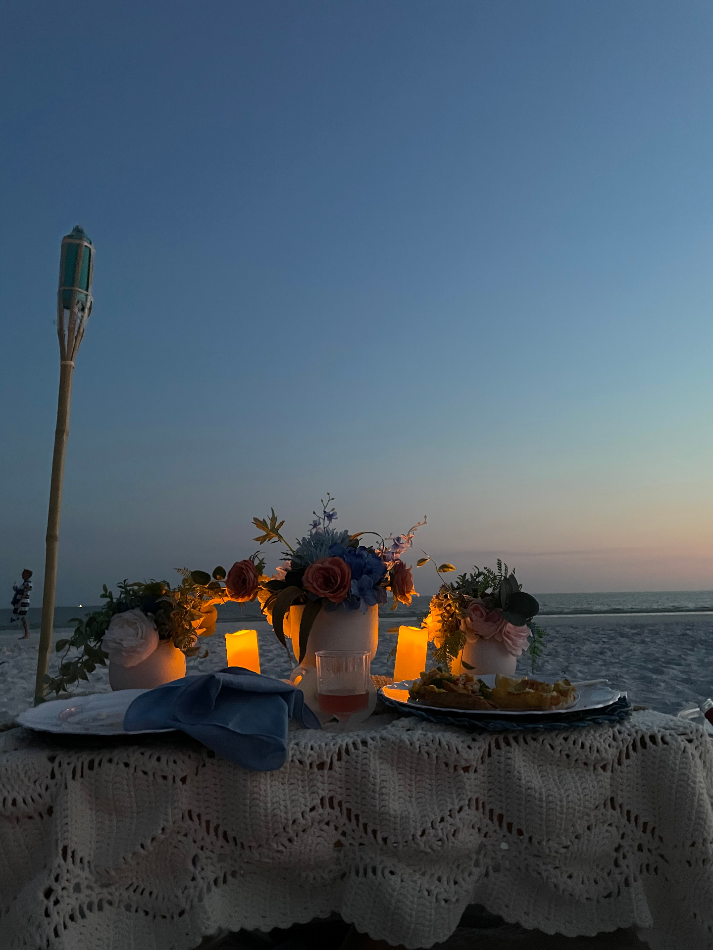 Candlelit table on the sand at dusk with flowers and tacos