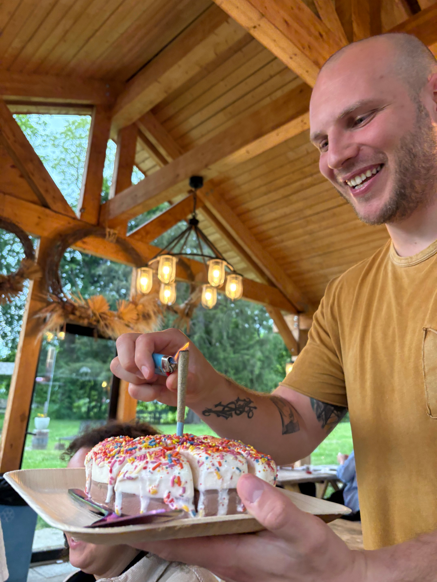 Lighting the candle on a sprinkle-covered cake under a wooden pavilion