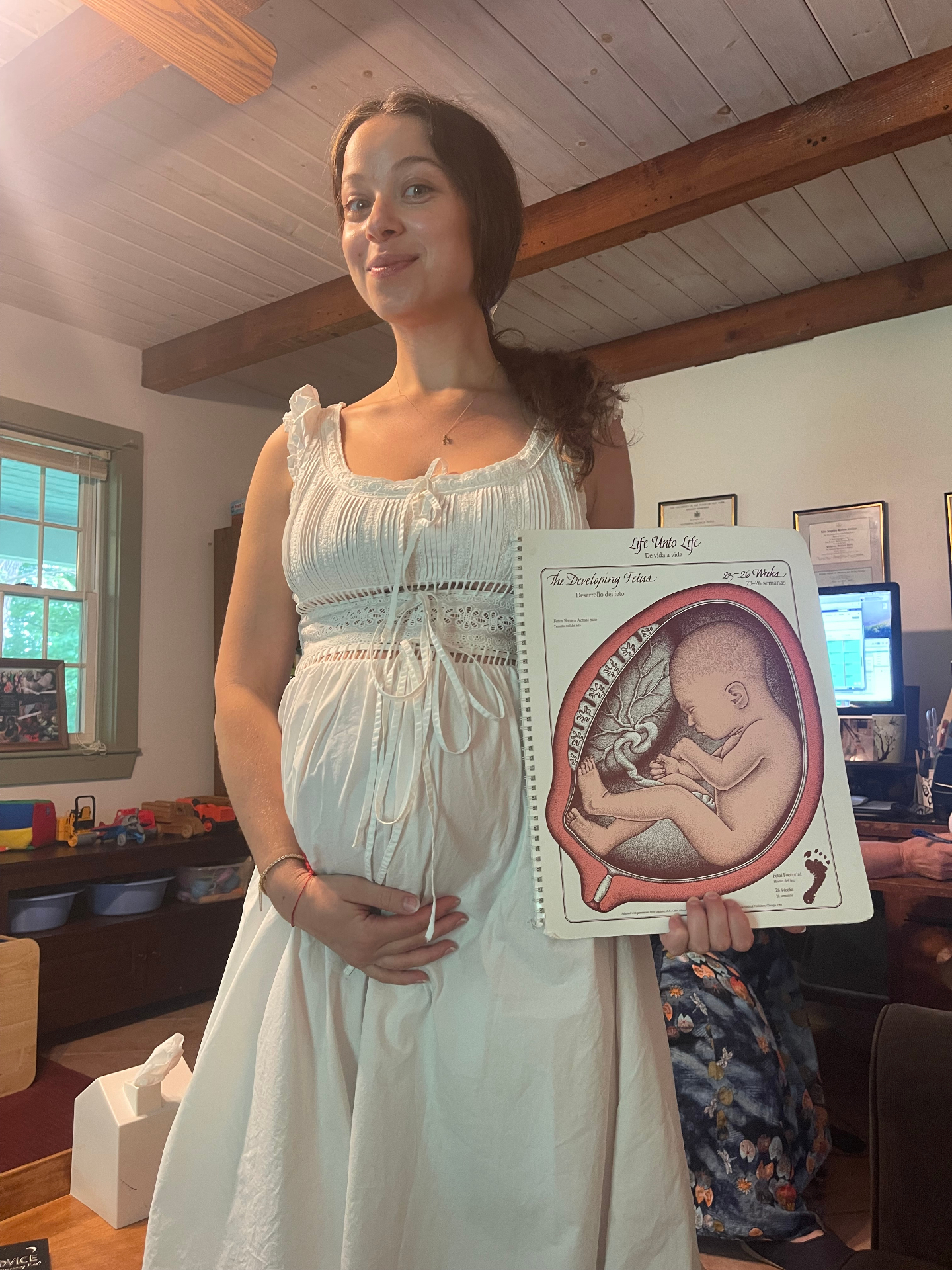 Noa pregnant, holding a fetal development chart