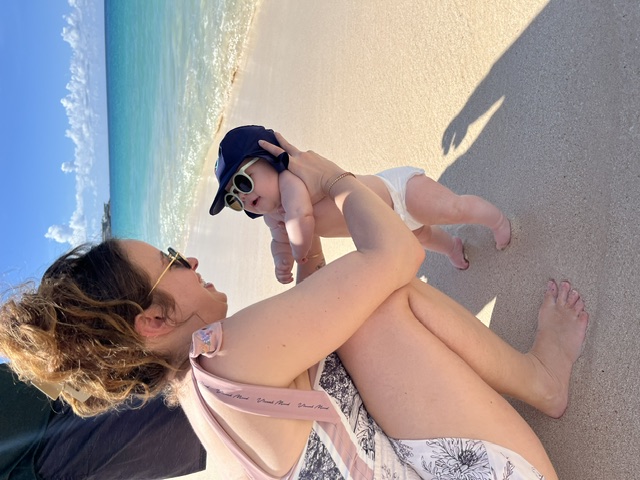 Noa crouched on the sand holding Oren by the waves