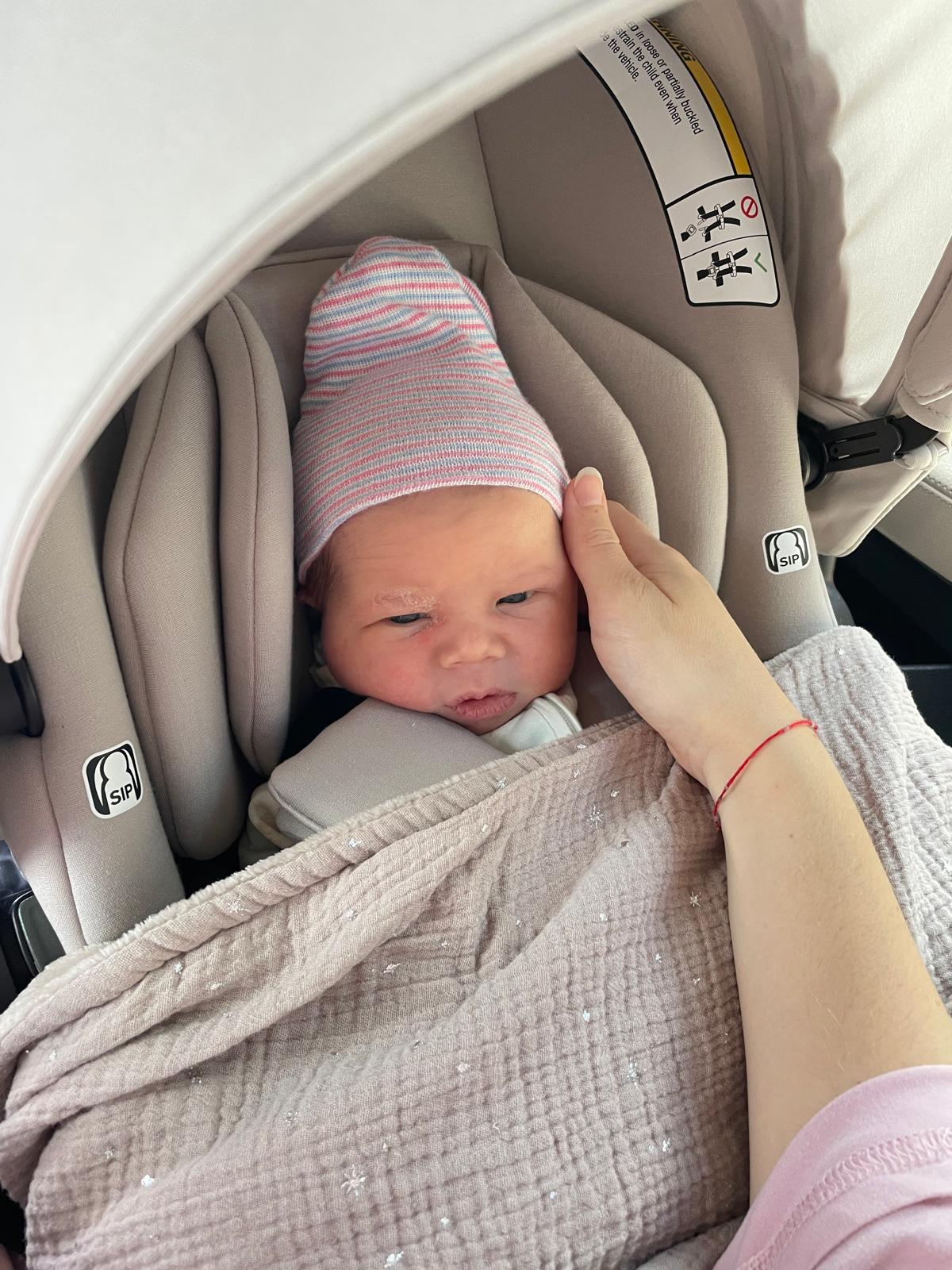 Newborn Oren in a striped hat in his car seat, Noa's hand resting on his head