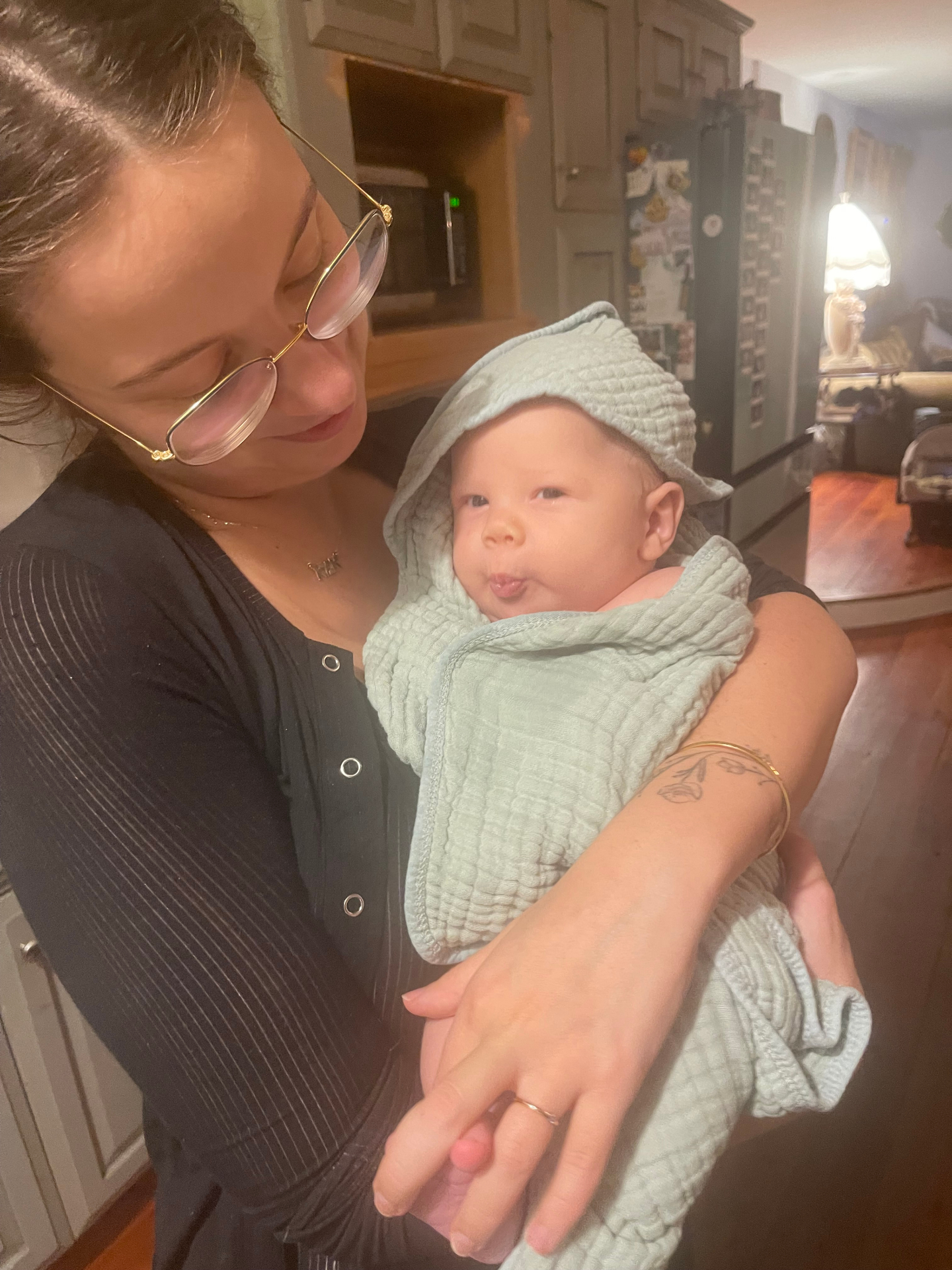 Noa holding Oren wrapped in a sage green swaddle